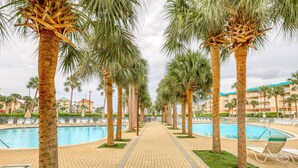 A pool area with palm trees, lounge chairs, and a tiled walkway. - Fourth-floor, ocean-view condo with pool, high-speed WiFi, beach access & W&D (Miramar Beach)