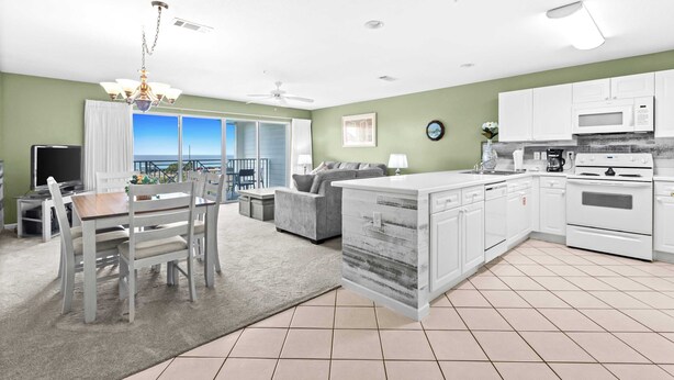 A modern kitchen with white cabinets, a central island, and a dining area with a view. - Fourth-floor, ocean-view condo with pool, high-speed WiFi, beach access & W&D (Miramar Beach)