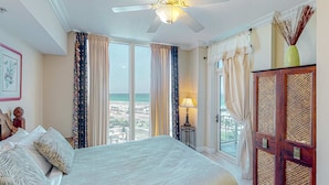 Une chambre d’hôtel avec un grand lit, un ventilateur de plafond, une vue sur la plage et une armoire en bois.