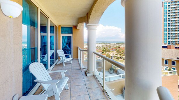 Un balcon avec des chaises blanches, une porte vitrée et une vue sur le paysage urbain.