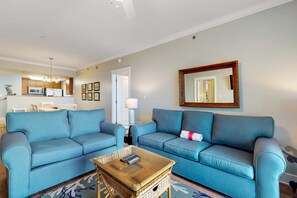 A living room with two blue sofas, a wooden coffee table, and a kitchen in the background. - Beachview Condo with full kitchen, shared pool and beach access (Fort Walton Beach)