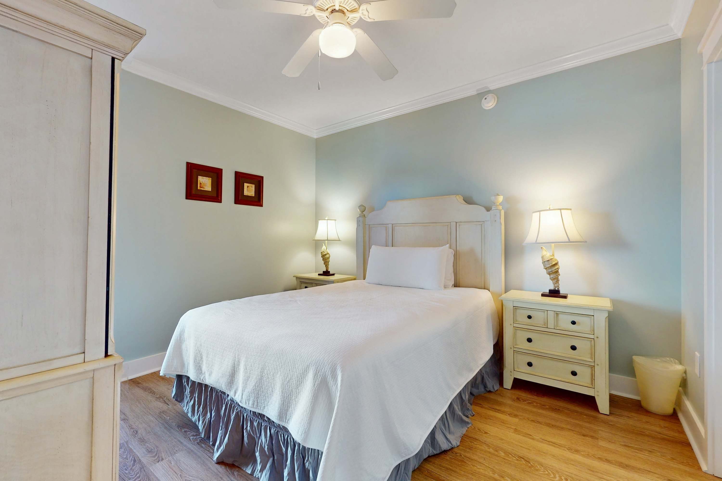 A bedroom with a bed, two bedside tables, a ceiling fan, and a nightstand with a lamp.