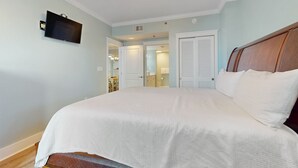 A bedroom with a large bed, a ceiling fan, a mounted TV, and a door leading to a bathroom. - Beachview Condo with full kitchen, shared pool and beach access (Fort Walton Beach)