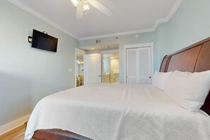 A bedroom with a large bed, a ceiling fan, a mounted TV, and a door leading to a bathroom. - Beachview Condo with full kitchen, shared pool and beach access (Fort Walton Beach)