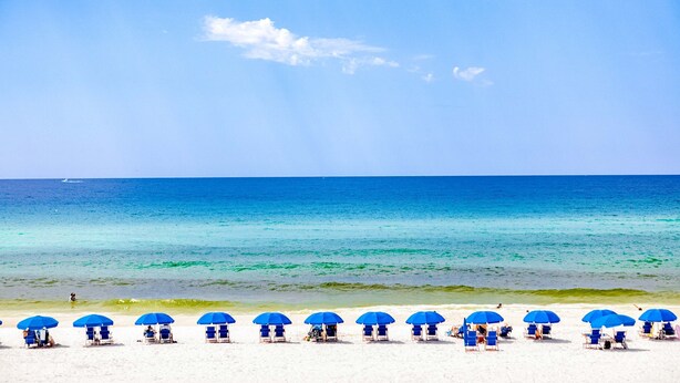 Ein Strand mit blauen Sonnenschirmen und weißen Liegestühlen.