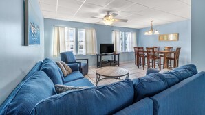 Un salon avec un grand canapé bleu, une petite table basse, un téléviseur et un coin repas comprenant des chaises et une table.