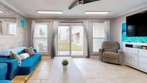 Una sala de estar moderna con un sofá azul, un sillón gris, un televisor de pantalla plana y un ventilador de techo.