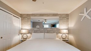 Un dormitorio con una cama grande, dos lámparas de noche, un ventilador de techo y una decoración de estrella de mar en la pared.