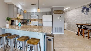 Una cocina moderna con encimeras de granito, electrodomésticos de acero inoxidable y taburetes de bar.