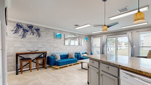 Una cocina moderna con refrigerador empotrado, una zona de comedor con sofá azul y taburetes de madera, y un ventilador de techo.