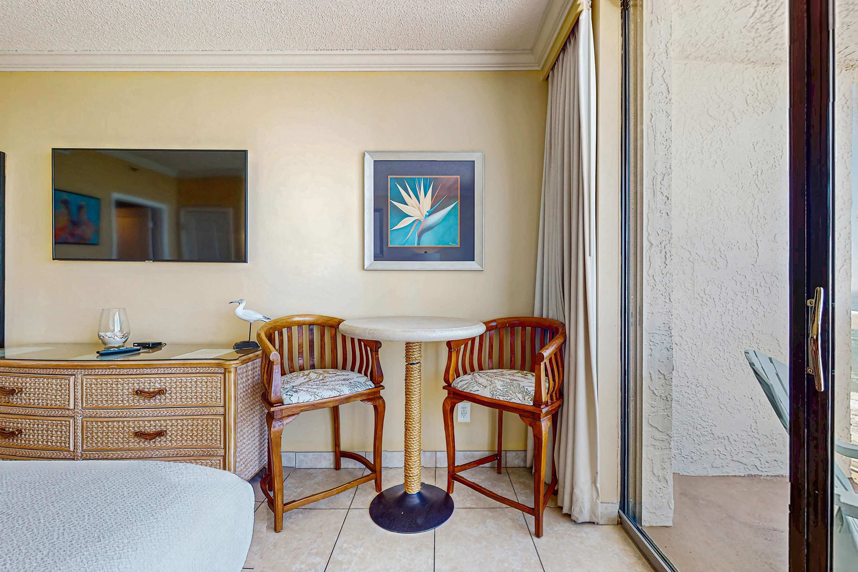 Hotelkamer met een bed, een houten dressoir, een ronde tafel met twee stoelen, een lijst met een afbeelding aan de muur en een raam met gordijnen.