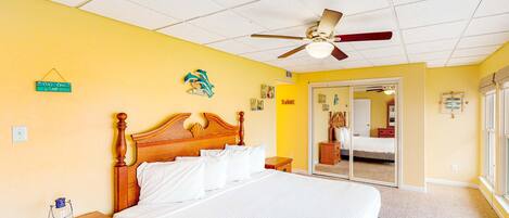 Een slaapkamer met een houten bed, een plafondventilator, een nachtkastje en een deur naar een andere kamer.