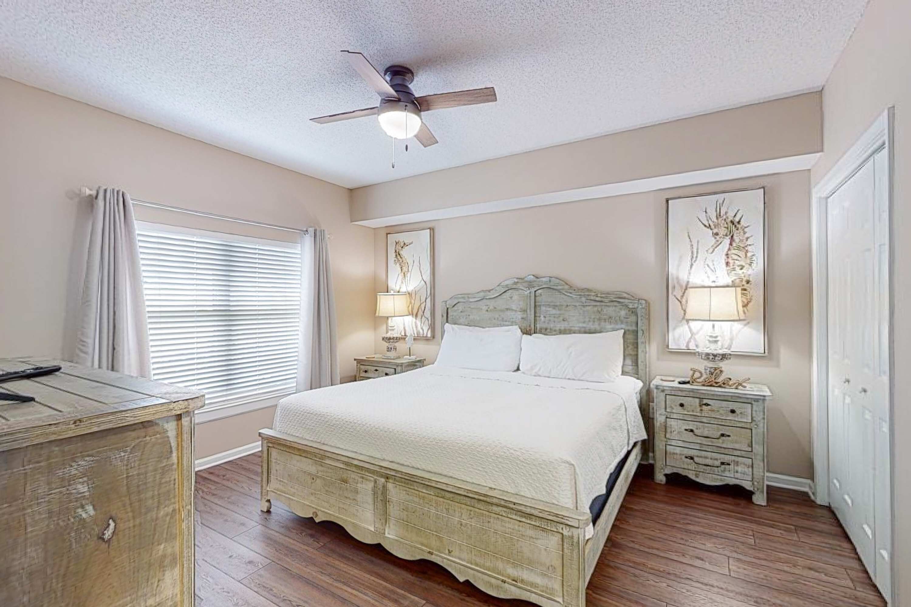 A bedroom with a large bed, two bedside tables with lamps, a ceiling fan, and a wooden dresser.