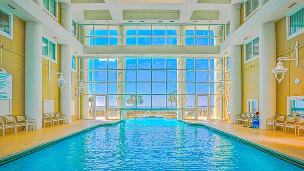 Una piscina interior con agua cristalina azul, ventanas amplias y ambiente iluminado por el sol.