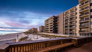 En træbro fører til et strandhotel med flere balkoner og havudsigt.