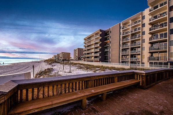 Un paseo marítimo de madera que conduce a un hotel frente al mar, con varios balcones y vistas al océano.