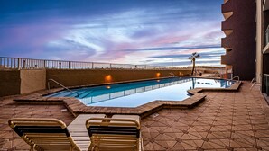 Pool på taget med liggestole, palmetræ og udsigt til solnedgang.