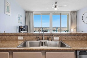 A kitchen with a double sink, a ceiling fan, and a view of the balcony. - Ground floor, oceanfront condo with pool, fast WiFi & seasonal beach service (Fort Walton Beach)