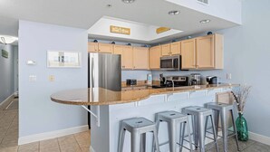 Uma cozinha moderna com uma ilha central, banquetas e um micro-ondas.