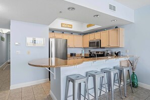 A modern kitchen with a central island, bar stools, and a microwave. - Ground floor, oceanfront condo with pool, fast WiFi & seasonal beach service (Fort Walton Beach)