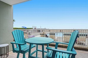 A balcony with turquoise chairs and a small table, overlooking a parking area and a clear sky. - Ground floor, oceanfront condo with pool, fast WiFi & seasonal beach service (Fort Walton Beach)