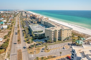 An aerial view of a coastal hotel with a beachside location, featuring a parking lot, a central building, and a beachfront promenade. - Gorgeous ground floor beachfront condo, shared pool and beach access (Fort Walton Beach)