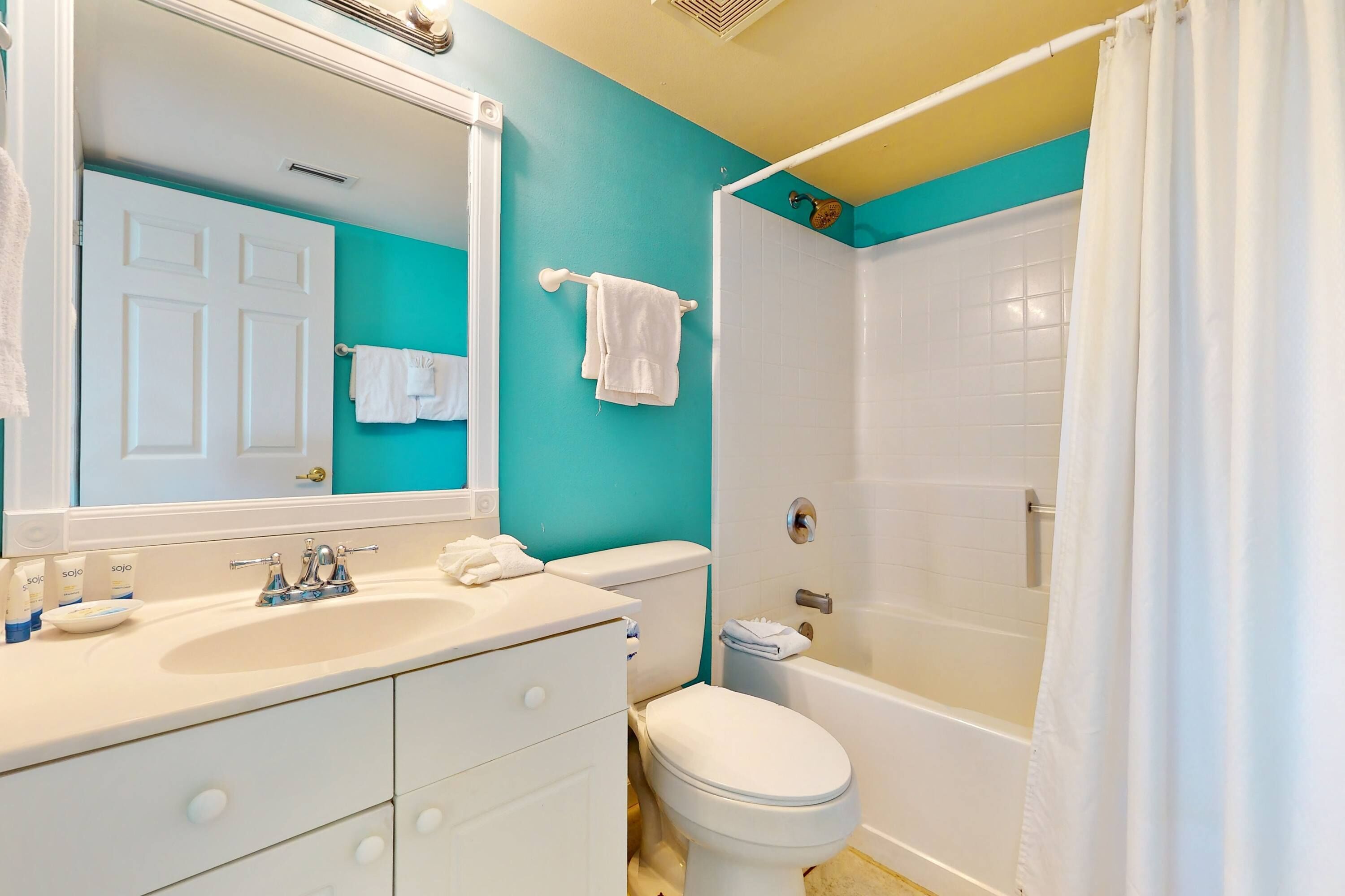 A bathroom with a white sink, toilet, and bathtub, and a teal accent wall.