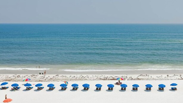 A beach with rows of blue and red beach umbrellas, white sand, and the ocean in the background. - Comfortable Vacation Rental On Okaloosa Island, On The Beach, On-Site Pool (Fort Walton Beach)