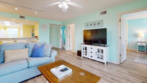 A living room with a light blue sofa, a wooden coffee table, a TV on a white cabinet, and a ceiling fan. - Comfortable Vacation Rental On Okaloosa Island, On The Beach, On-Site Pool (Fort Walton Beach)