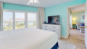 A bedroom with a large bed, a ceiling fan, a TV, and a view of the outdoors. - Comfortable Vacation Rental On Okaloosa Island, On The Beach, On-Site Pool (Fort Walton Beach)