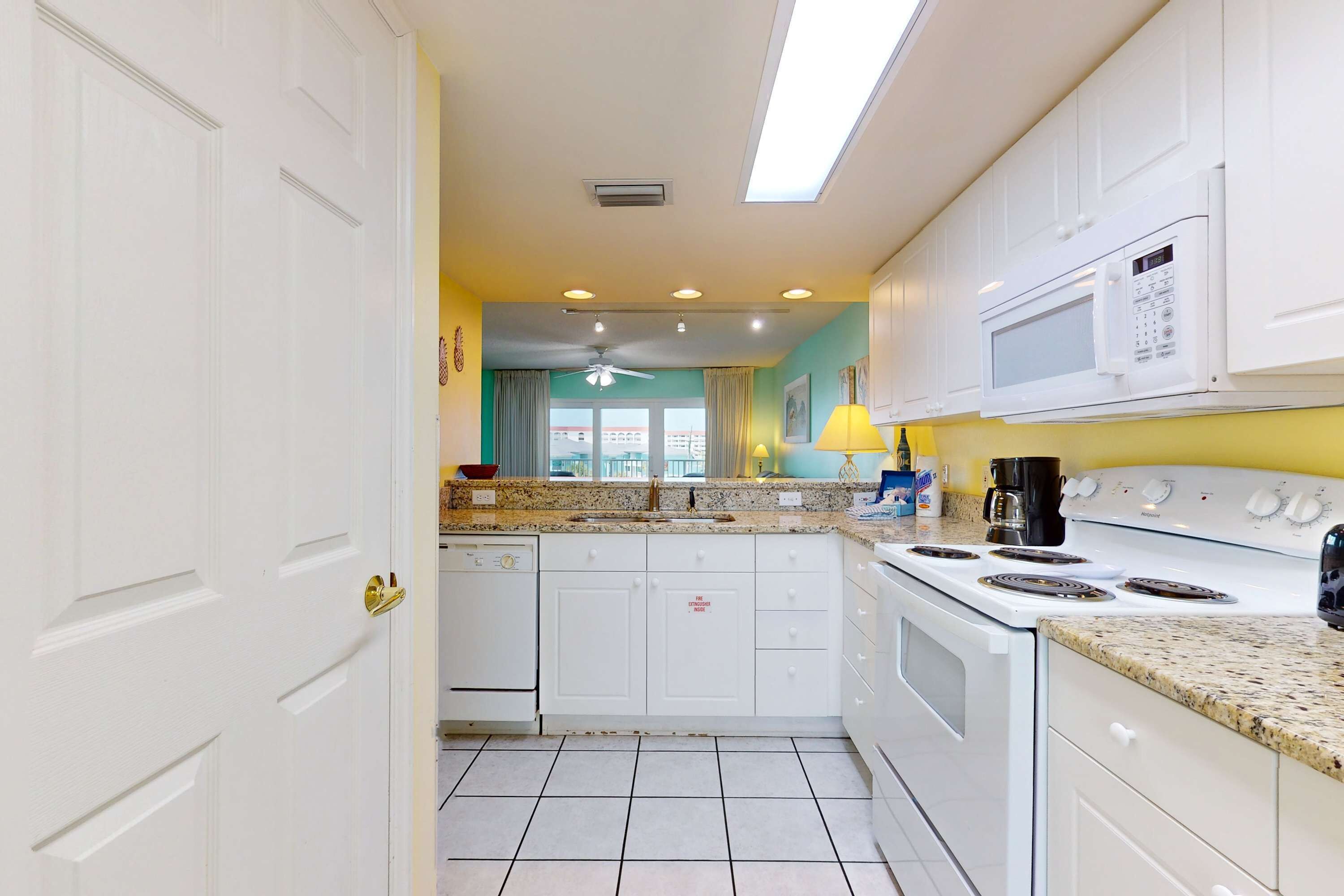 A kitchen with white cabinets, a stove, a microwave, and a window with curtains.
