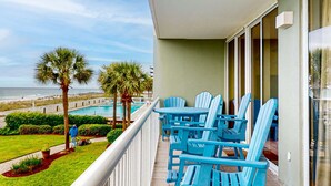 A balcony with blue Adirondack chairs, a pool, and a view of the beach. - Comfortable and cozy beachfront condo w shared amenities (Fort Walton Beach)
