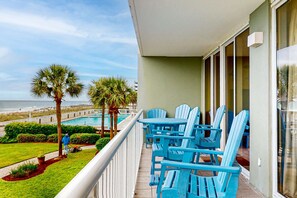 A balcony with blue Adirondack chairs, a pool, and a view of the beach. - Comfortable and cozy beachfront condo w shared amenities (Fort Walton Beach)