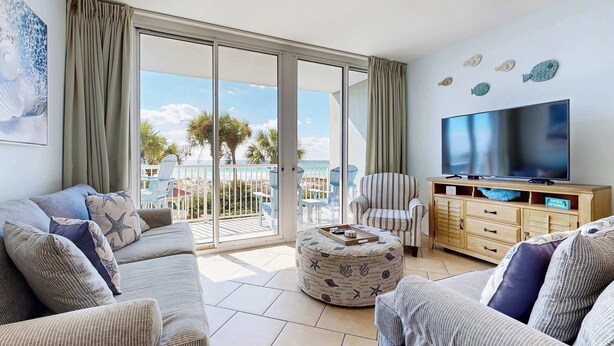 A living room with a sofa, ottoman, TV, and a view of the outdoors. - Comfortable and cozy beachfront condo w shared amenities (Fort Walton Beach)