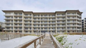Een meerlaags hotel met balkons, een houten looppad naar de ingang en een zandstrand.