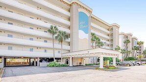 Een hotel met meerdere verdiepingen, met een opvallend bord met de naam 'Gulf Dunes', een overdekte ingang en een parkeerplaats met meerdere auto's.