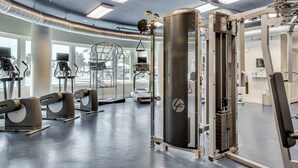 Une salle de sport moderne équipée de divers appareils d’exercice, dotée de grandes fenêtres et d’un intérieur propre et bien éclairé.