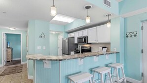 Una cocina con una isla central, taburetes de bar y electrodomésticos modernos.