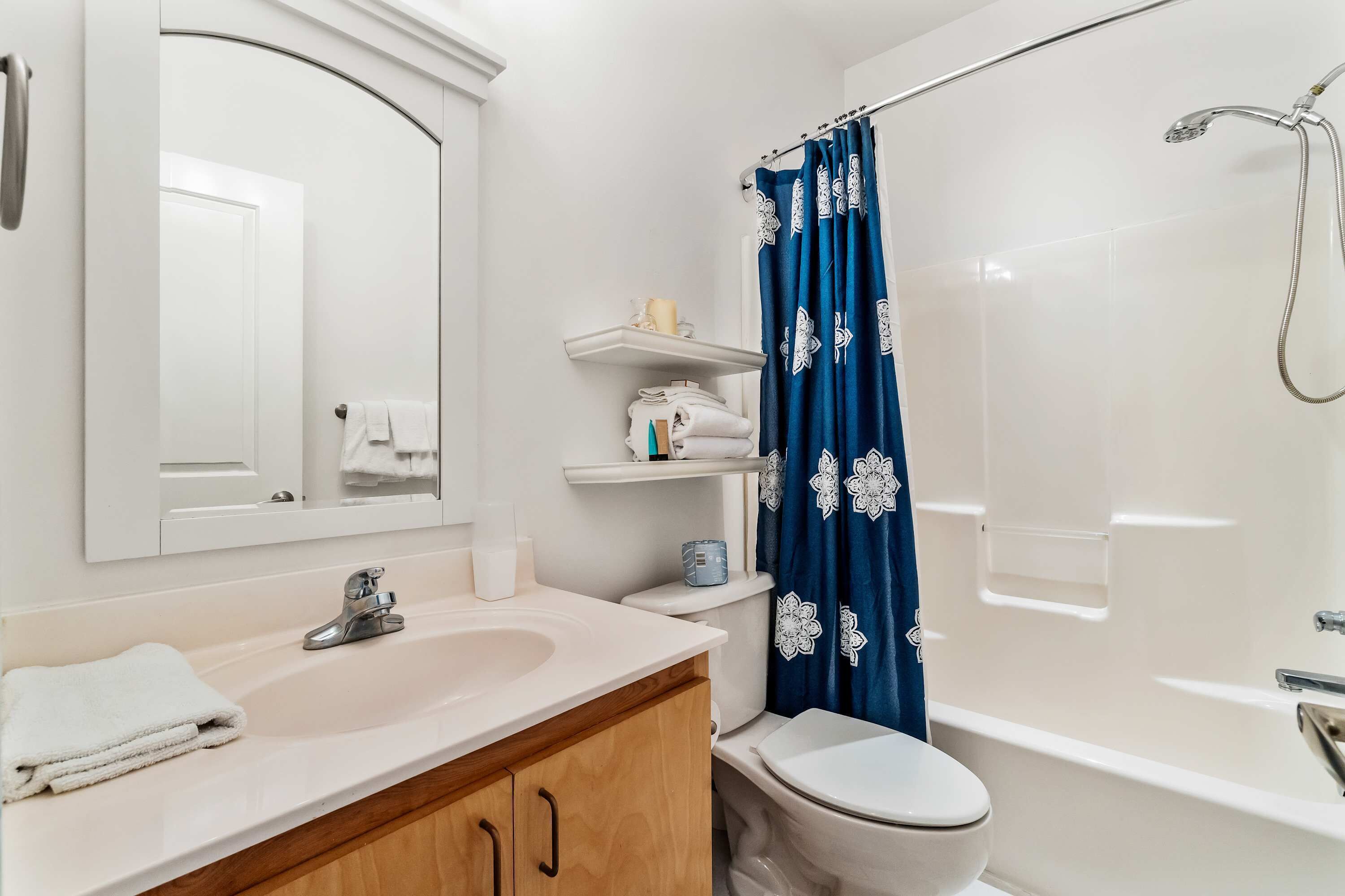 Ein Badezimmer mit Waschbecken, Spiegel und Toilette, einem blauen Duschvorhang und einer weißen Badewanne.