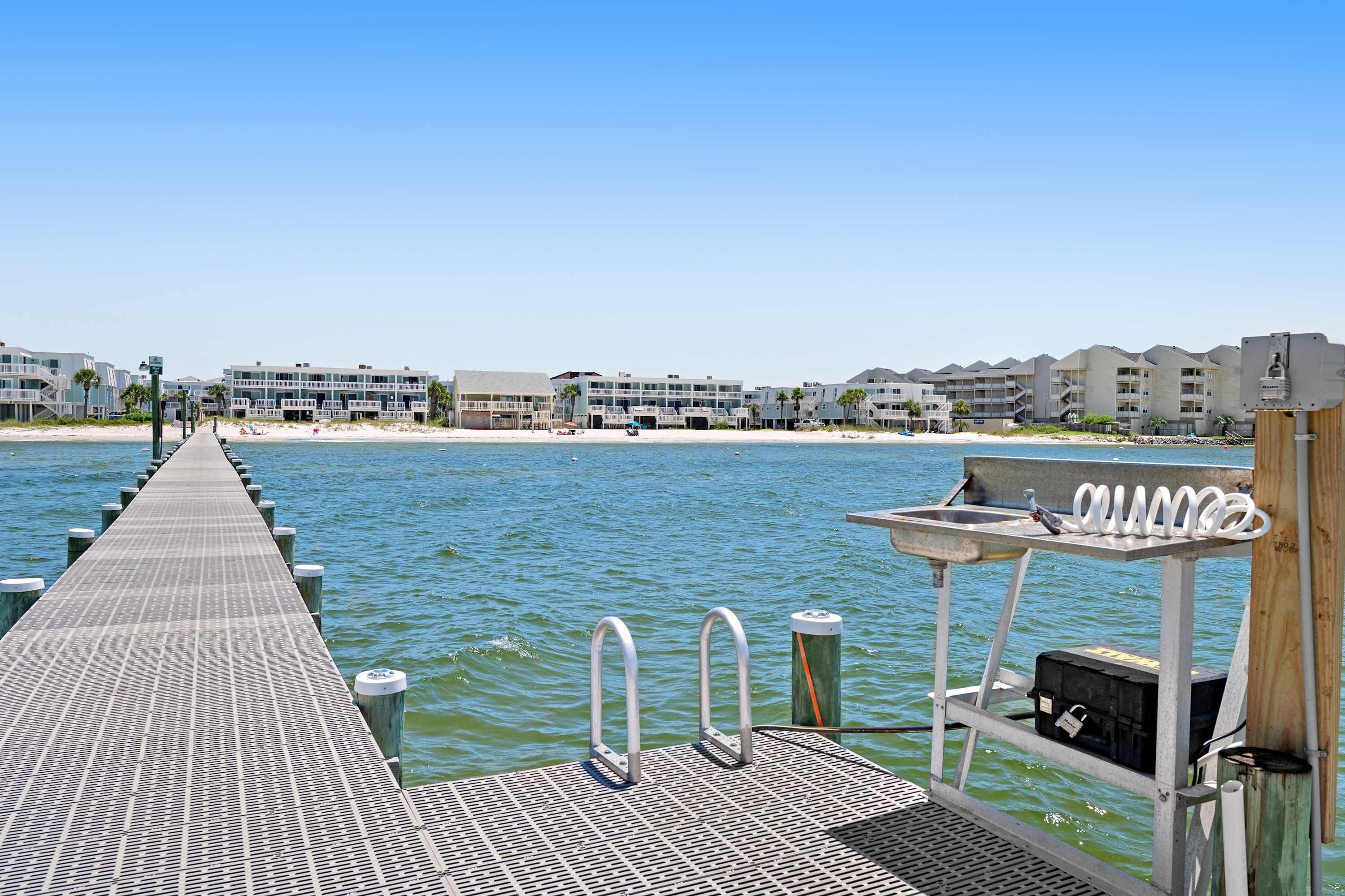 A pier extending into calm water with a row of buildings in the background.