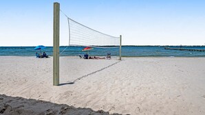 Ein Beachvolleyballnetz mit sandigem Strand und einem Pier im Hintergrund.