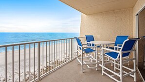 Un balcon avec vue sur la plage et l’océan. On y trouve des chaises blanches et une table.