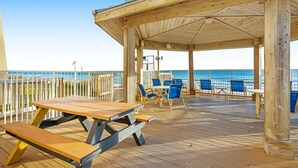 A wooden deck with picnic tables and chairs, overlooking a beach. - Beachfront ground-floor condo with beach & Gulf views, outdoor pool & tennis (Miramar Beach)