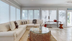 Un salón amplio con un sofá seccional beige grande, una mesa de centro de vidrio y una pequeña mesita auxiliar de madera.
