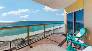 Un balcón con vista a la playa y al océano, sillas turquesas y una mesa.
