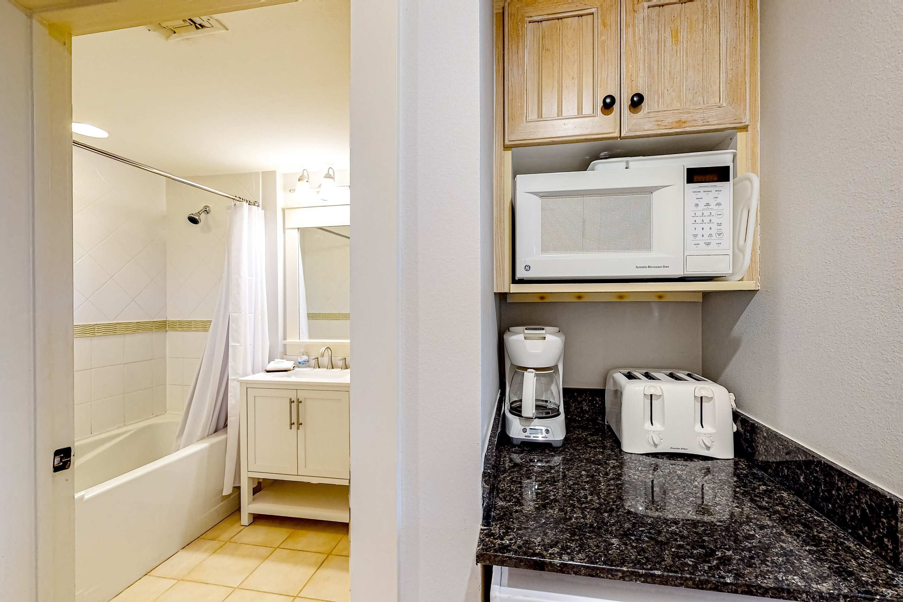 A bathroom with a shower, a toilet, a sink, and a cabinet with a microwave and toaster.