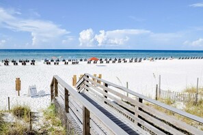 A beach with a wooden boardwalk leading to the water, white sand, and umbrellas.