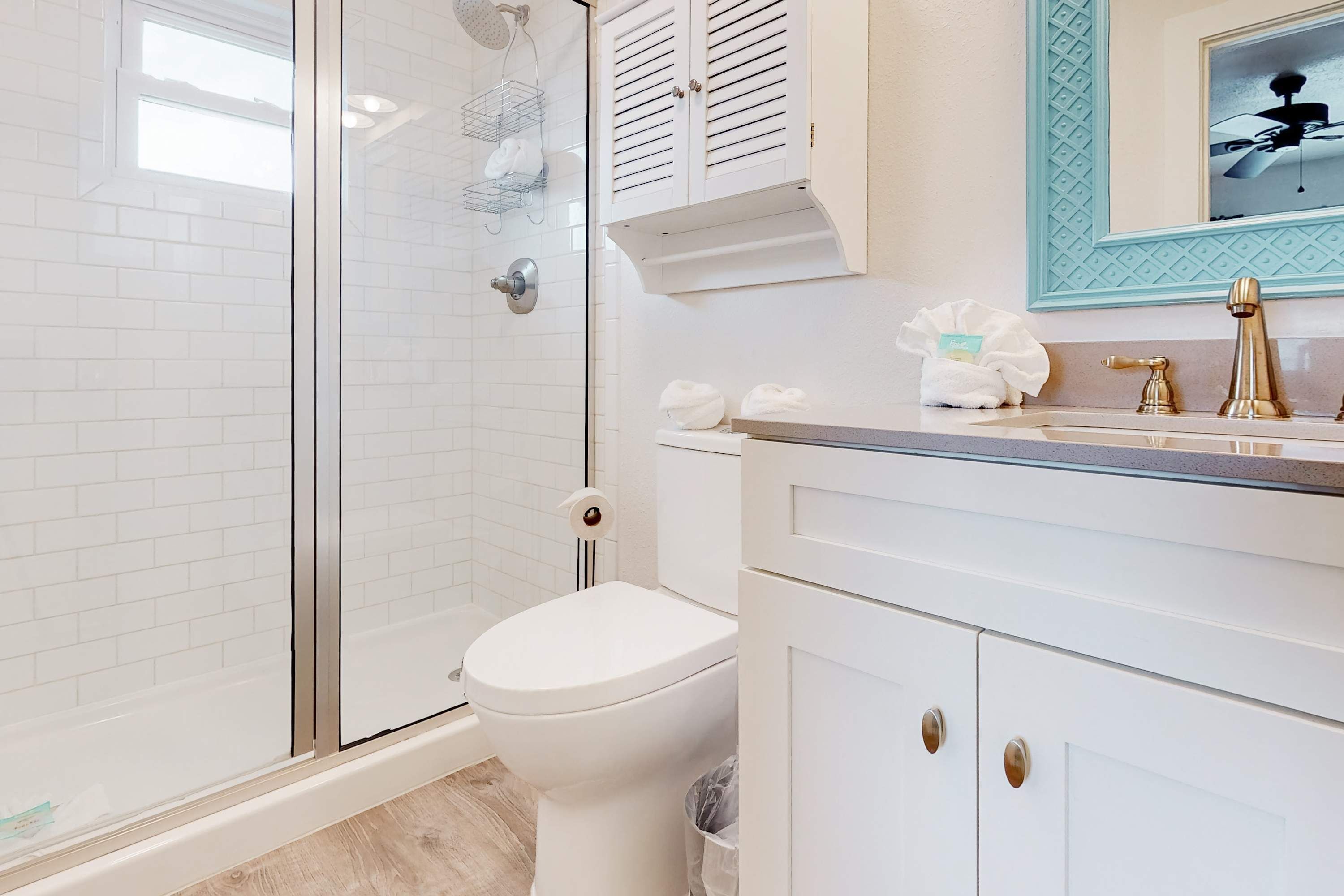 Une salle de bain moderne avec une douche à parois de verre, des murs recouverts de carreaux blancs, des toilettes blanches et un meuble-lavabo avec des accessoires dorés.
