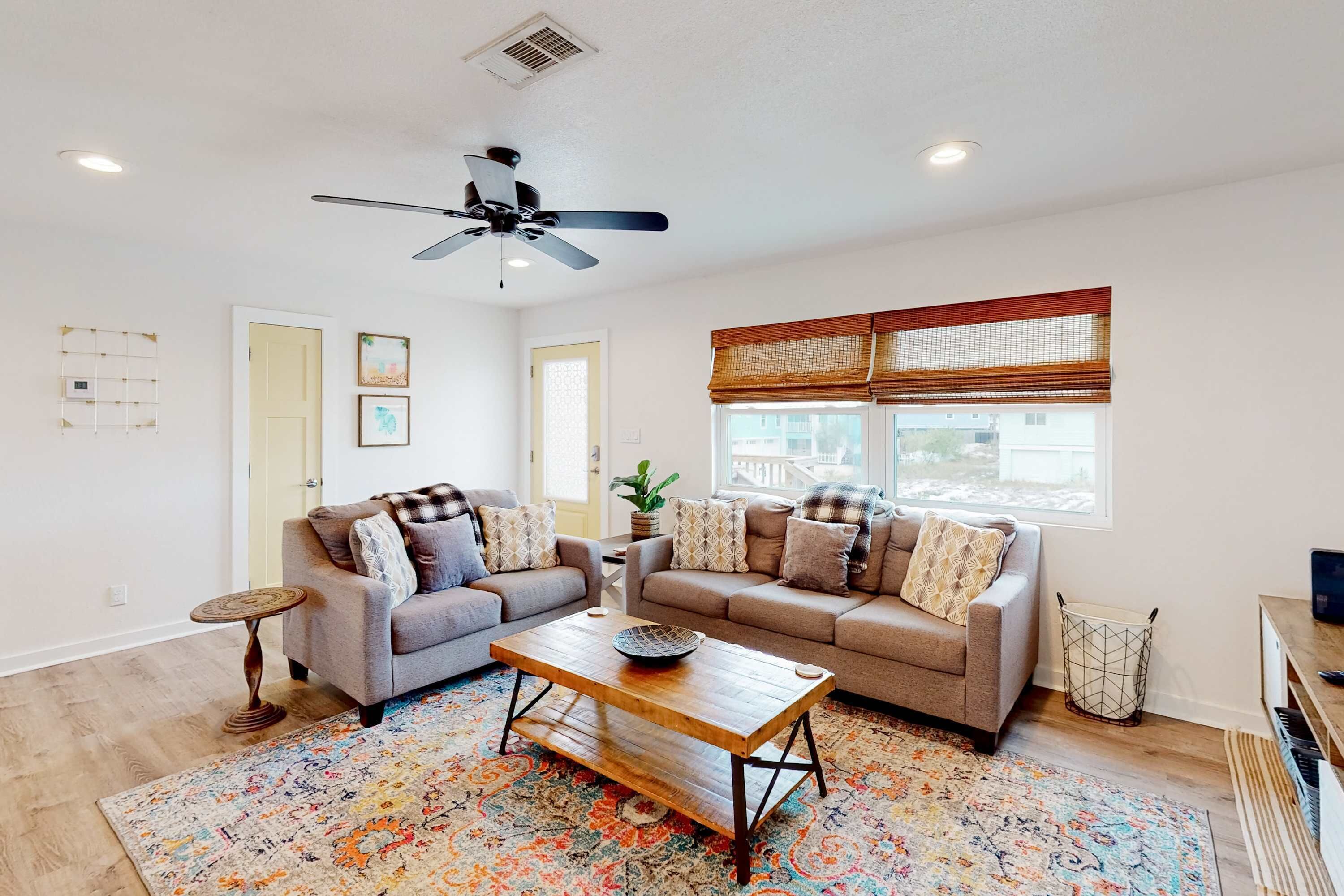 A living room with two sofas, a coffee table, a ceiling fan, and a window with blinds.