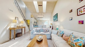 Ein geräumiges Wohnzimmer mit einem Holztisch, einem hellen Sofa und einer Treppe, die zu einer oberen Etage führt.